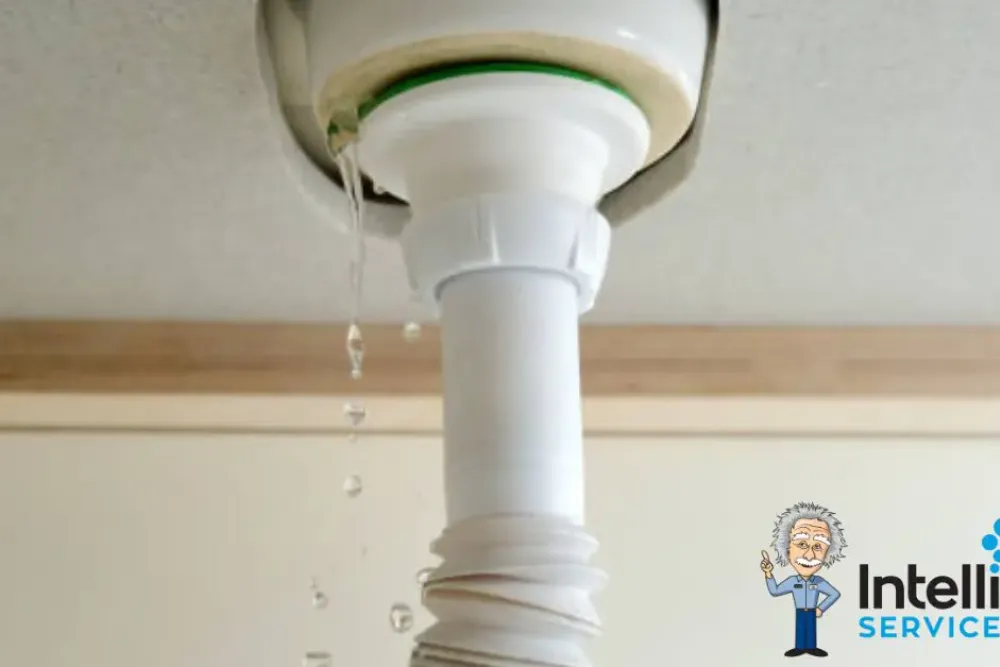 Leaking drain pipe under sink, highlighting plumbing issue with Intelligent Service logo.
