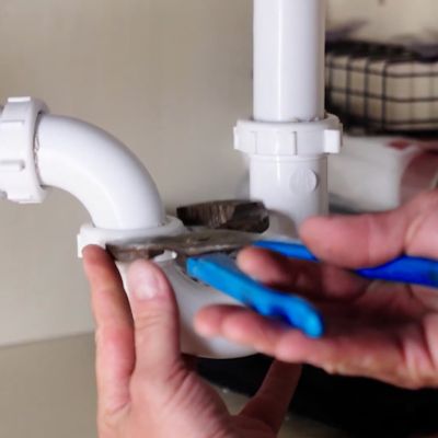 Hands using wrench to fix white sink pipe, demonstrating plumbing repair and maintenance skills.