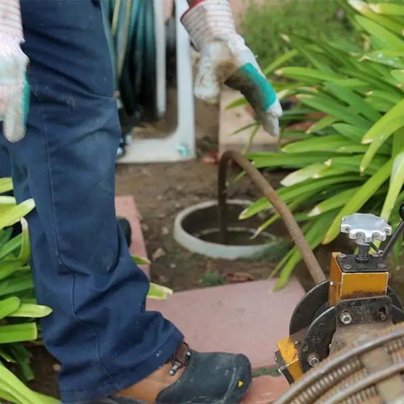 Worker using drain cleaning machine in garden area for plumbing maintenance.
