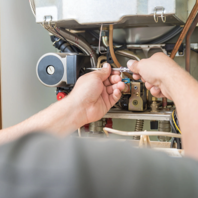 Technician repairing a boiler with a screwdriver, focusing on pipes and components.